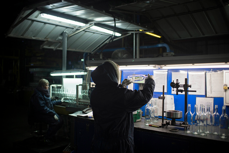 An employee checks the quality of glass bottles on the production line.